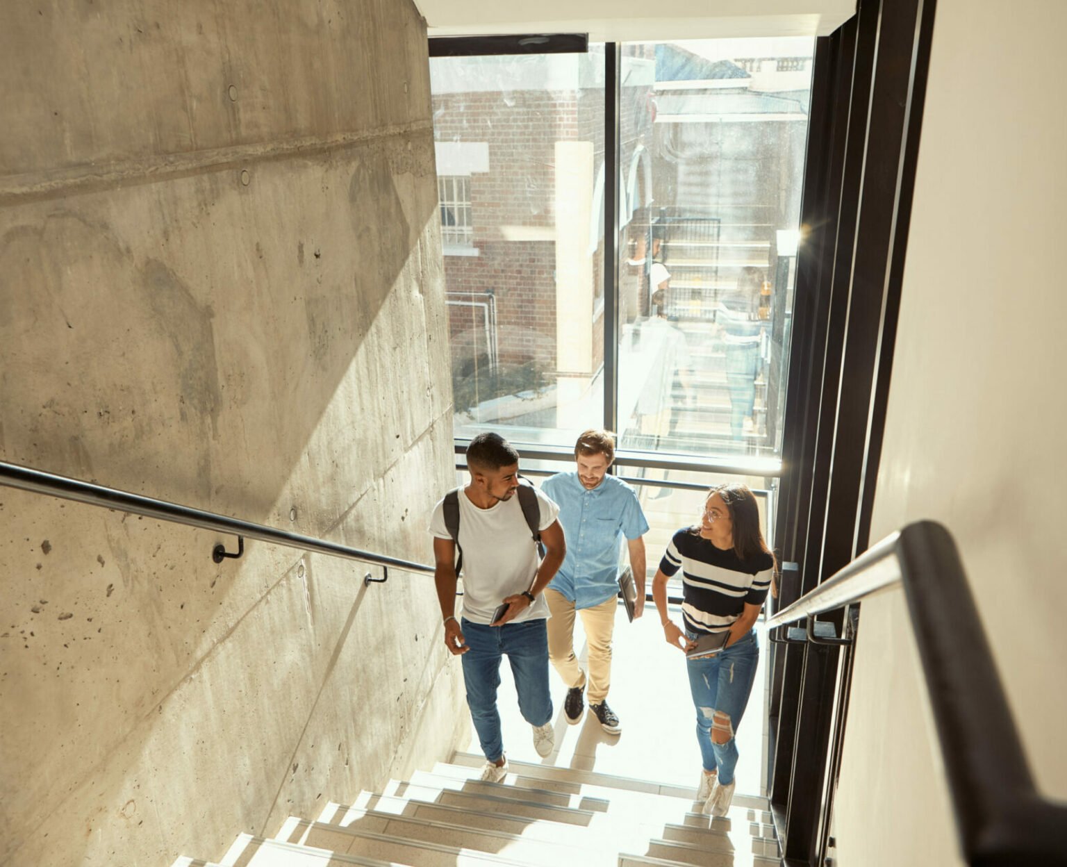 Bilde av en gruppe unge studenter/elever som går opp en trapp i et moderne bygg.